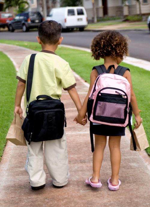 students holding hands while carrying lunch bags and wearing backpacks